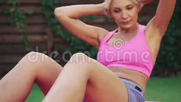 年轻的运动女子训练躺在绿草地上的腹肌视频的预览图