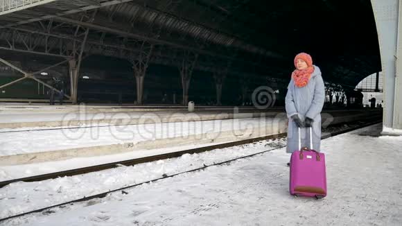 清晨一个旅客妇女拿着紫色的行李站在火车站等待火车视频的预览图