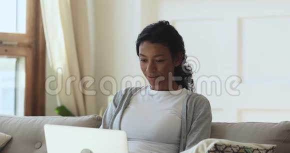 快乐的年轻非裔美国女人用手提电脑坐在沙发上视频的预览图