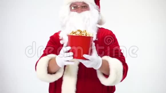 白色背景上的圣诞老人带着一桶红色的爆米花吃爆米花和看电影提供爆米花视频的预览图