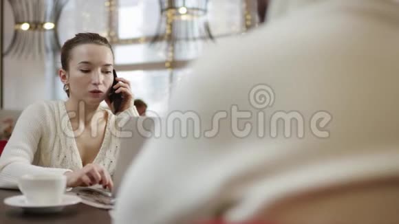 年轻的女商人坐在笔记本电脑前的桌子旁一边谈论着智能手机一边看着坐着的男人视频的预览图