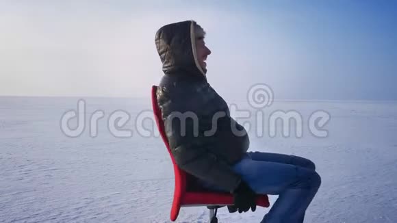 穿着暖和的外套戴着兜帽在雪地里旋转着红色的椅子视频的预览图