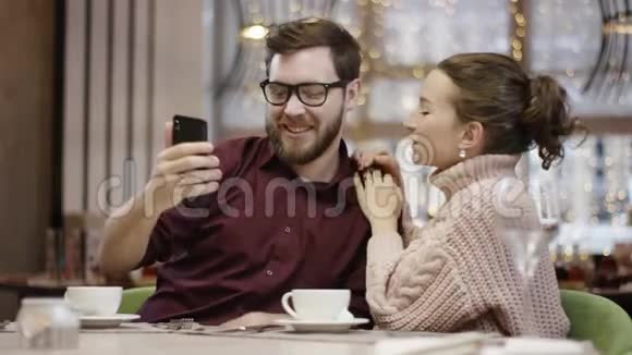 一对快乐的情侣在餐厅里用智能手机和餐桌边傻笑视频的预览图