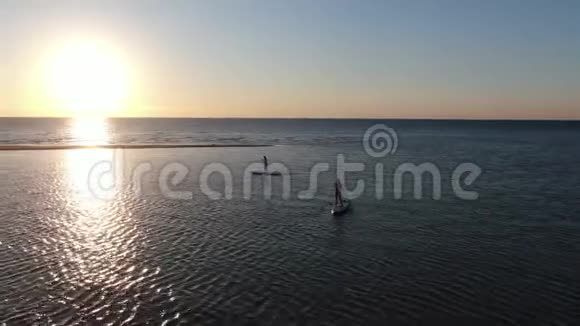 年轻的女人站在木板上在大海上划桨日落4K视频的预览图