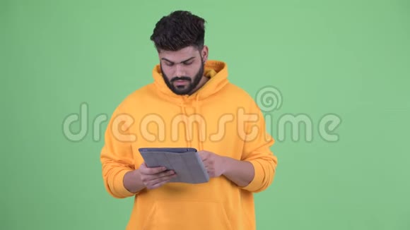 快乐年轻体重超重留着胡子的印度男人在用数码平板电脑思考视频的预览图