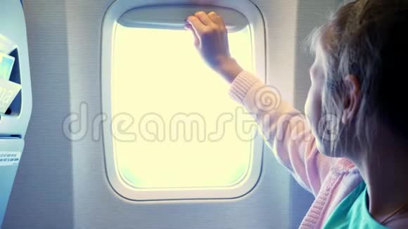 特写镜头小女孩把舷窗窗帘放在飞机的机舱里从那里发出明亮的光一个女孩视频的预览图