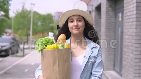 一个年轻漂亮的女人穿着牛仔夹克和帽子带着一个购物袋心情愉快微笑着视频的预览图