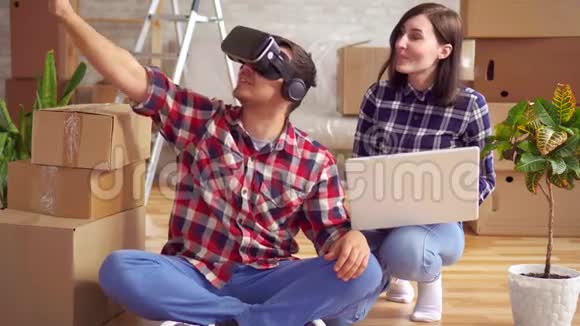 带笔记本电脑的女人展示了一个戴着虚拟现实眼镜的男人的新公寓项目视频的预览图