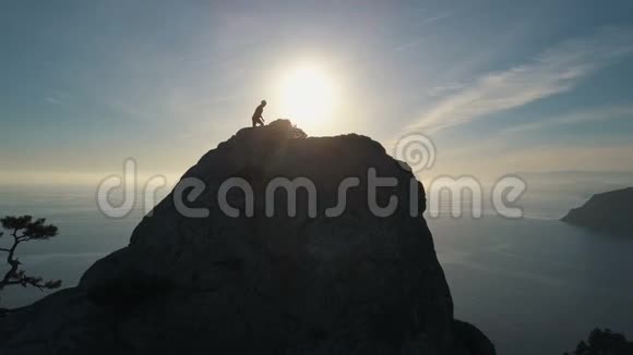 夕阳西下一位年轻女子爬上山顶靠海的空中轮廓出席峰会的女士视频的预览图