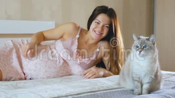 一个孕妇醒来抚摸着她的腹部猫坐在她旁边的床上女孩微笑着看着视频的预览图