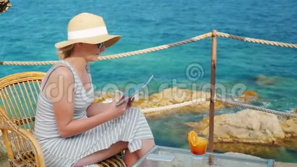 商务女性度假坐在一家咖啡馆里有着美丽的海景它可以用平板电脑视频的预览图