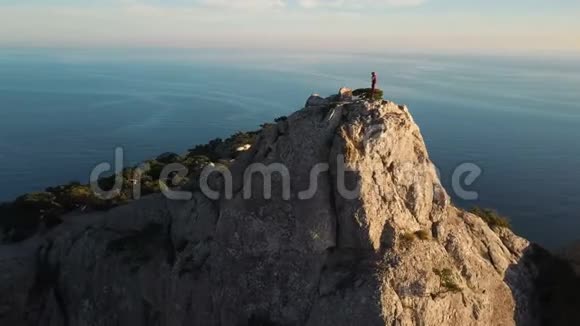 夕阳西下一位年轻女子爬上山顶靠海的空中轮廓出席峰会的女士视频的预览图