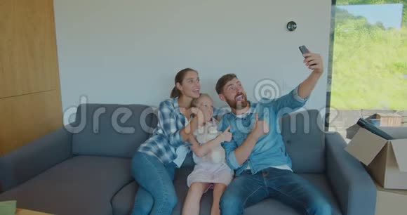 美丽的家庭在智能手机上做令人难忘的自拍同时放松一次又一次地坐在纸板箱之间视频的预览图