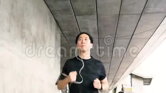 年轻的亚洲人在城里跑步戴着耳机视频的预览图