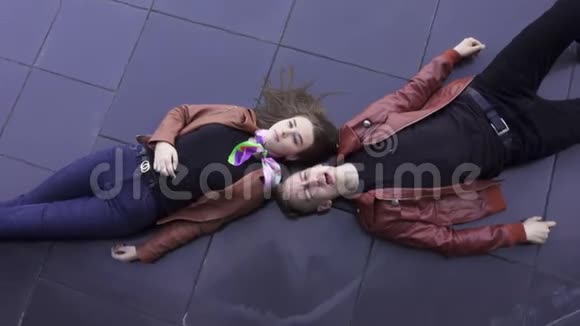 可爱的歌唱家和穿着浅棕色夹克的漂亮女孩躺在深色瓷砖地板上视频的预览图