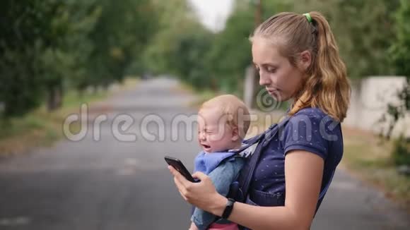 有孩子的现代年轻母亲使用手机视频的预览图