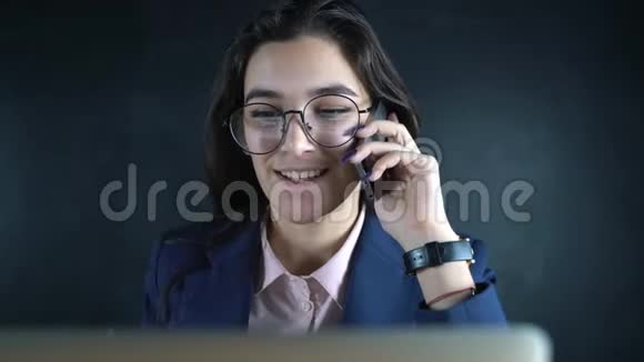 年轻的女经理用手机在商务办公室用笔记本电脑说话商业女性使用手机视频的预览图