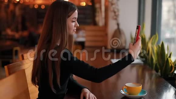 女人坐在咖啡馆里用智能手机自拍视频的预览图