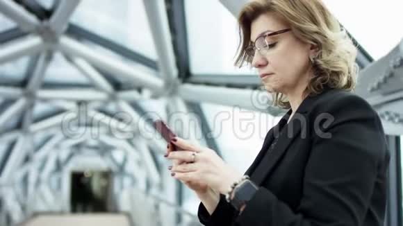 前台看到一个商务女性站着检查智能手机的内容然后停止她正在滚动监视器视频的预览图