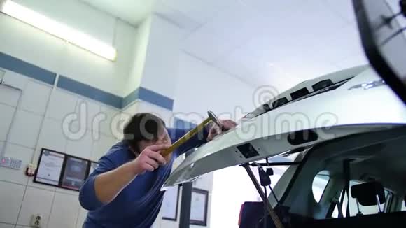 无油漆凹痕修复一个穿蓝色套头衫的人在一家汽车修理厂修理后备箱修补无油漆的凹痕视频的预览图