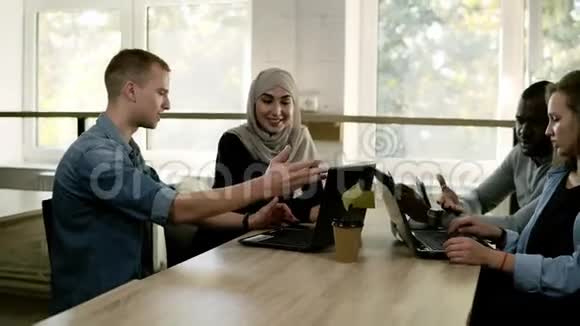 不同的人使用笔记本电脑而坐在窗前明亮的工作场所多种族和多文化视频的预览图