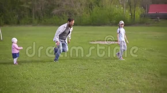 长胡子的父亲和两个女儿在体育场踢足球夏日绿草如茵视频的预览图