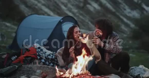 浪漫的时光一对夫妇一起在山上露营坐在篝火旁吃一些棉花糖视频的预览图