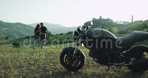浪漫的一对夫妇带着他们的黑色摩托车来到了美丽的风景中有着绿色的田野山和视频的预览图