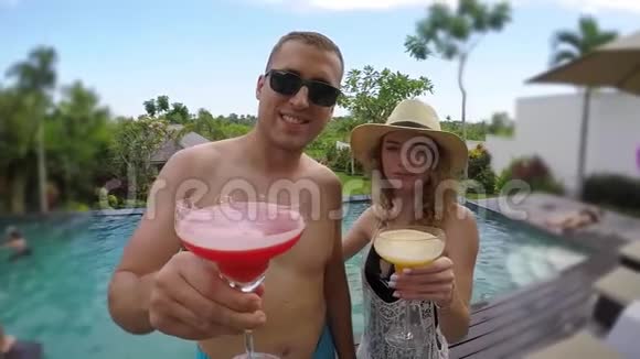 一对年轻可爱的夫妇在热带度假别墅的游泳池附近碰杯视频的预览图