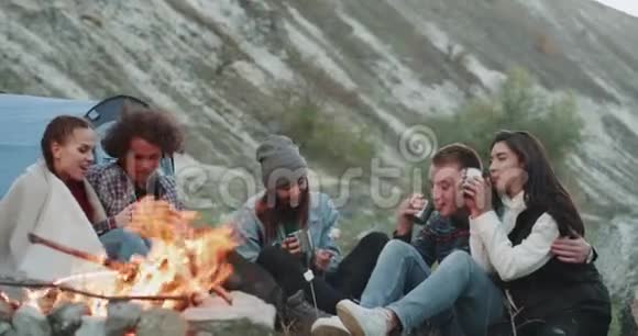 晚上在野营时多文化的青少年在一起很愉快坐在篝火旁喝茶视频的预览图