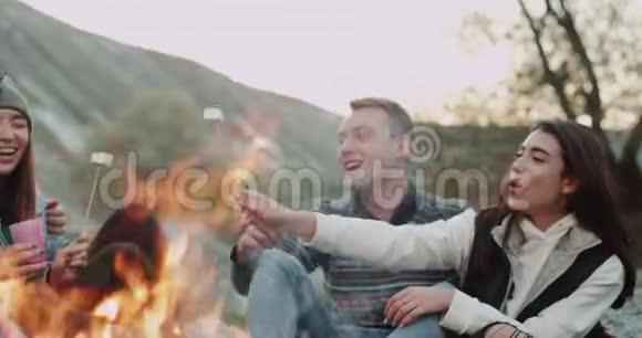 一群多元文化的朋友在露营时吃棉花糖在篝火旁喝酒视频的预览图