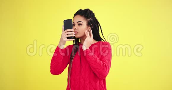 美丽的非洲年轻女子用智能手机在摄影棚里拍摄自己的照片照片背景为黄色视频的预览图