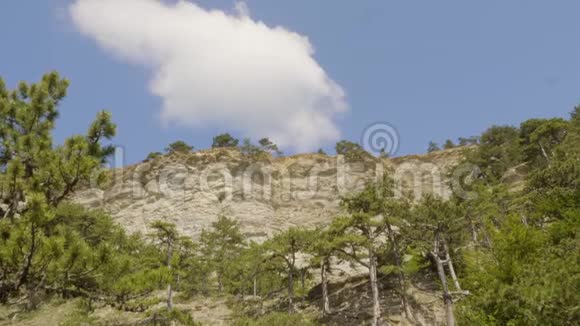 白云漂浮在岩石悬崖上覆盖着绿树从云下看高山上晴朗的蓝天视频的预览图