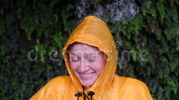 微笑的女人在倾盆大雨中穿着黄色雨衣慢动作的肖像视频的预览图