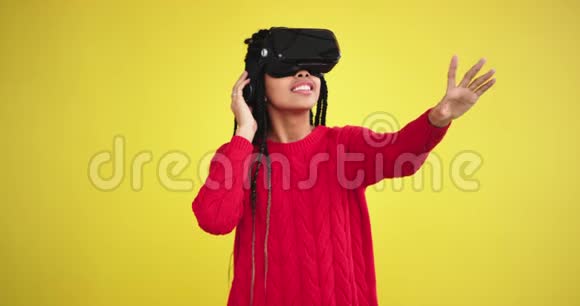 一位穿着红色上衣的非洲女士用虚拟现实眼镜在一个黄色背景的工作室里玩耍在前面视频的预览图