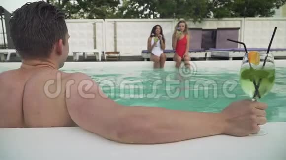 在两个漂亮女孩的背景下湿漉漉的年轻人从露天游泳池出来A视频的预览图
