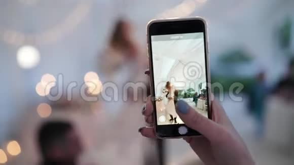 年轻夫妇的婚礼舞新娘和新郎在帐篷里的聚会上跳舞在手机上拍视频视频的预览图