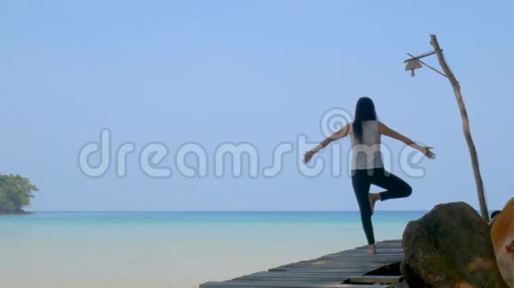 4K暑假期间一个女人站在一条腿上在海上的木桥上练习瑜伽亚洲年轻人视频的预览图