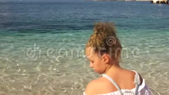 少女坐在沙滩上往水里扔石子美丽的大自然和清澈的绿松石水旅费视频的预览图