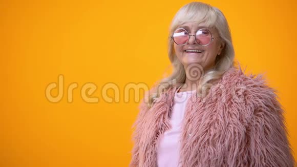 穿着粉红色外套和圆形太阳镜的开朗的高级女性玩得开心积极视频的预览图