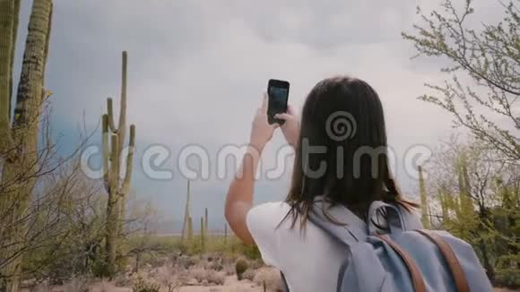 慢动作快乐的年轻成年旅游妇女在亚利桑那州国家公园拍摄巨大的Saguaro仙人掌的智能手机照片视频的预览图