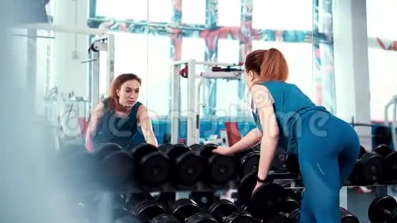 宽框年轻的健身女孩在一面巨大的镜子前用哑铃做运动视频的预览图