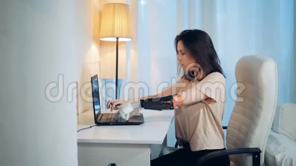 一位女士用她的机器人手在笔记本电脑上工作喝咖啡视频的预览图