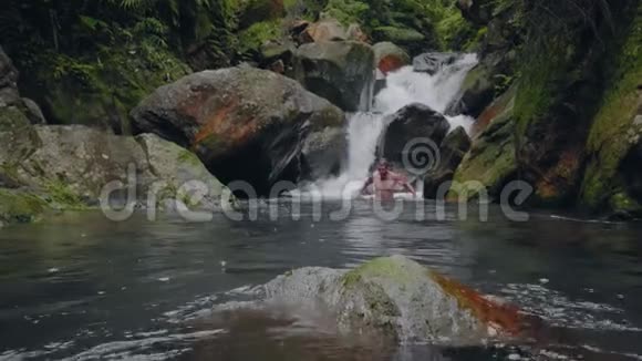 年轻人在热带森林中从瀑布流出来的河流中游泳旅行者在瀑布河里洗澡视频的预览图