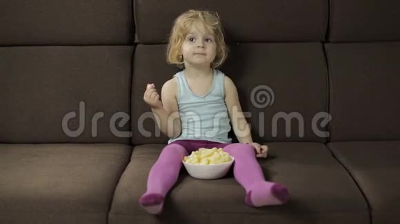 女孩坐在沙发上吃玉米泡芙儿童看电视品尝爆米花视频的预览图