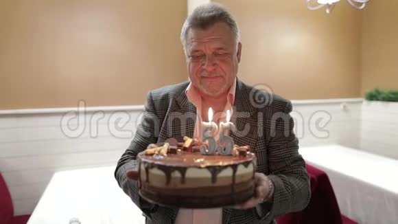 快乐可敬的老人拿着蛋糕庆祝一下吹生日蜡烛视频的预览图