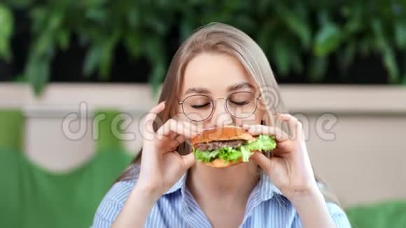 特写肖像快乐愉快年轻的女人吃美味的脂肪汉堡看着相机视频的预览图