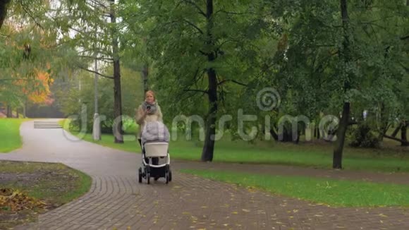 女人在秋天公园和婴儿散步时使用手机视频的预览图