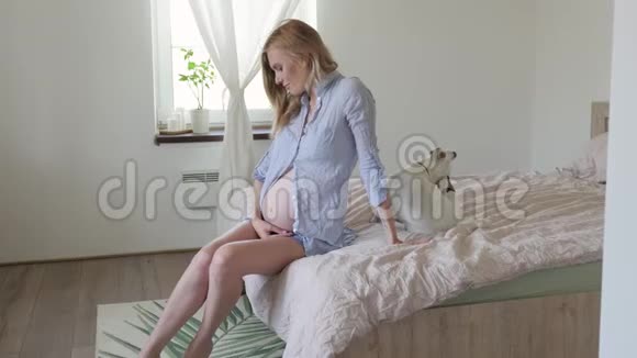 坐在床上的孕妇抚摸着她的腹部斯堪的纳维亚风格的内部视频的预览图
