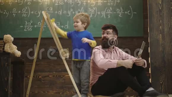 微笑的老师戴着眼镜看着孩子擦拭黑板父亲和兴奋的金发孩子学习数学侧视男孩和视频的预览图